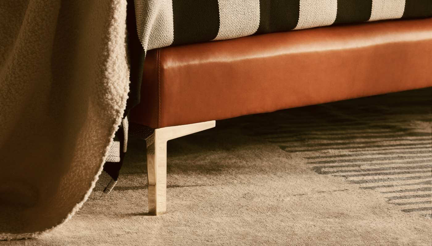 The box spring base of the Winston design, upholstered in cognac leather and paired with gold brass legs, dressed in stripped bedding
