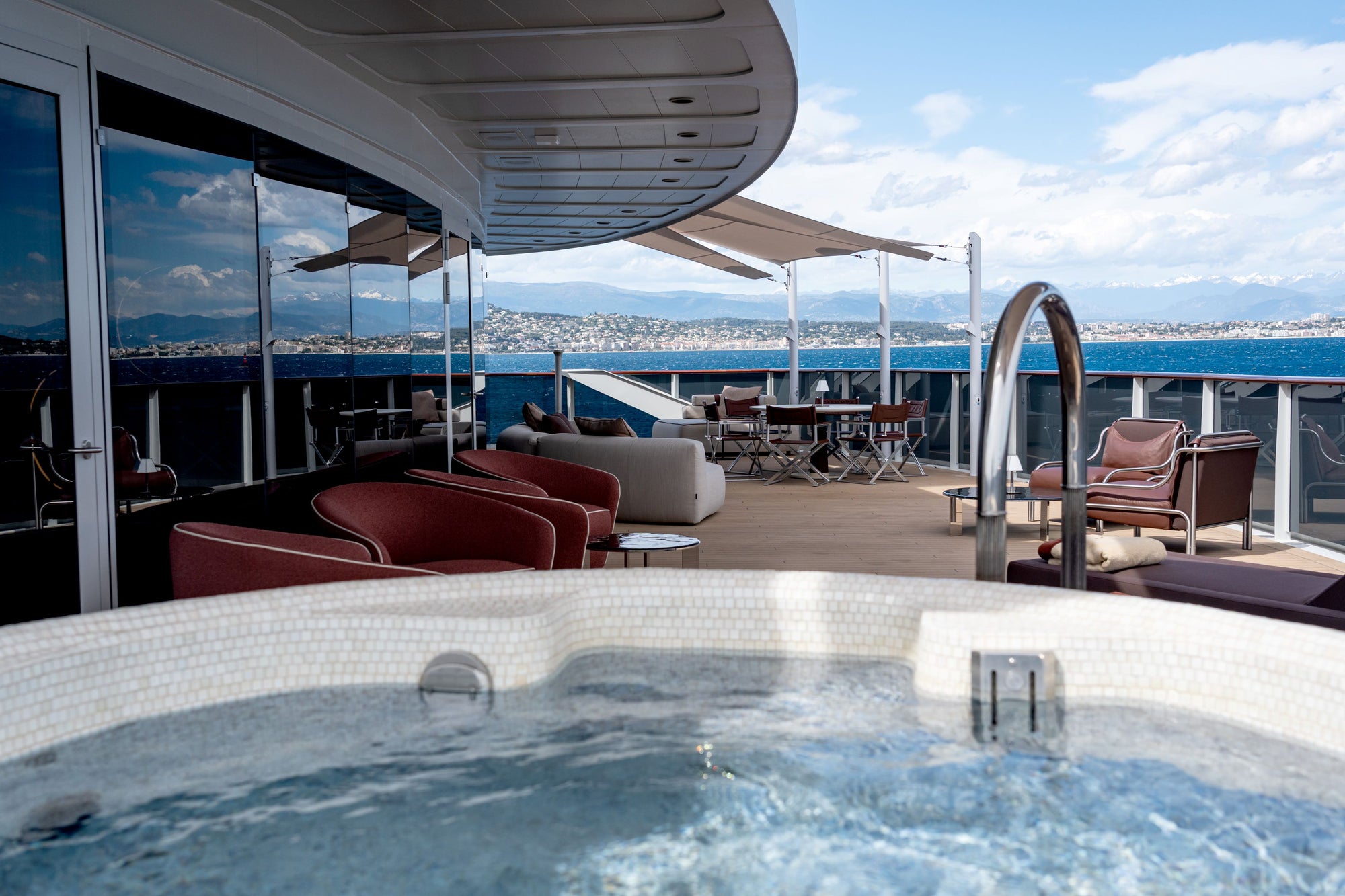 A swimming pool in the foreground on Orient Express Sailing Corinthian yacht deck with lounge chairs, and an ocean view in the background.