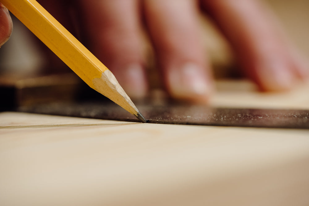 a Savoir craftsman using a pencil to draw a line on a piece of wood