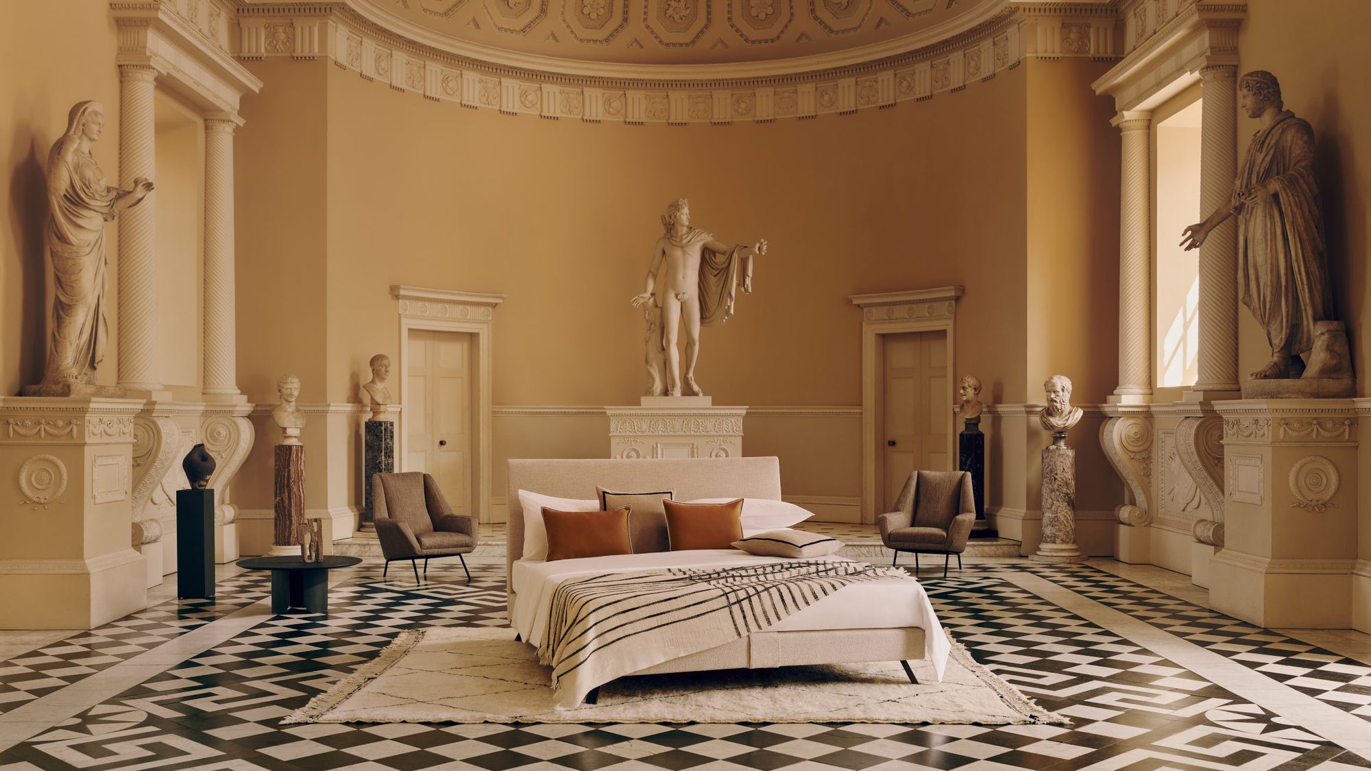 Savoir Ian bed with a beige headboard and striped blanket photographed facing a room full of Greek-style statues at The Syon House
