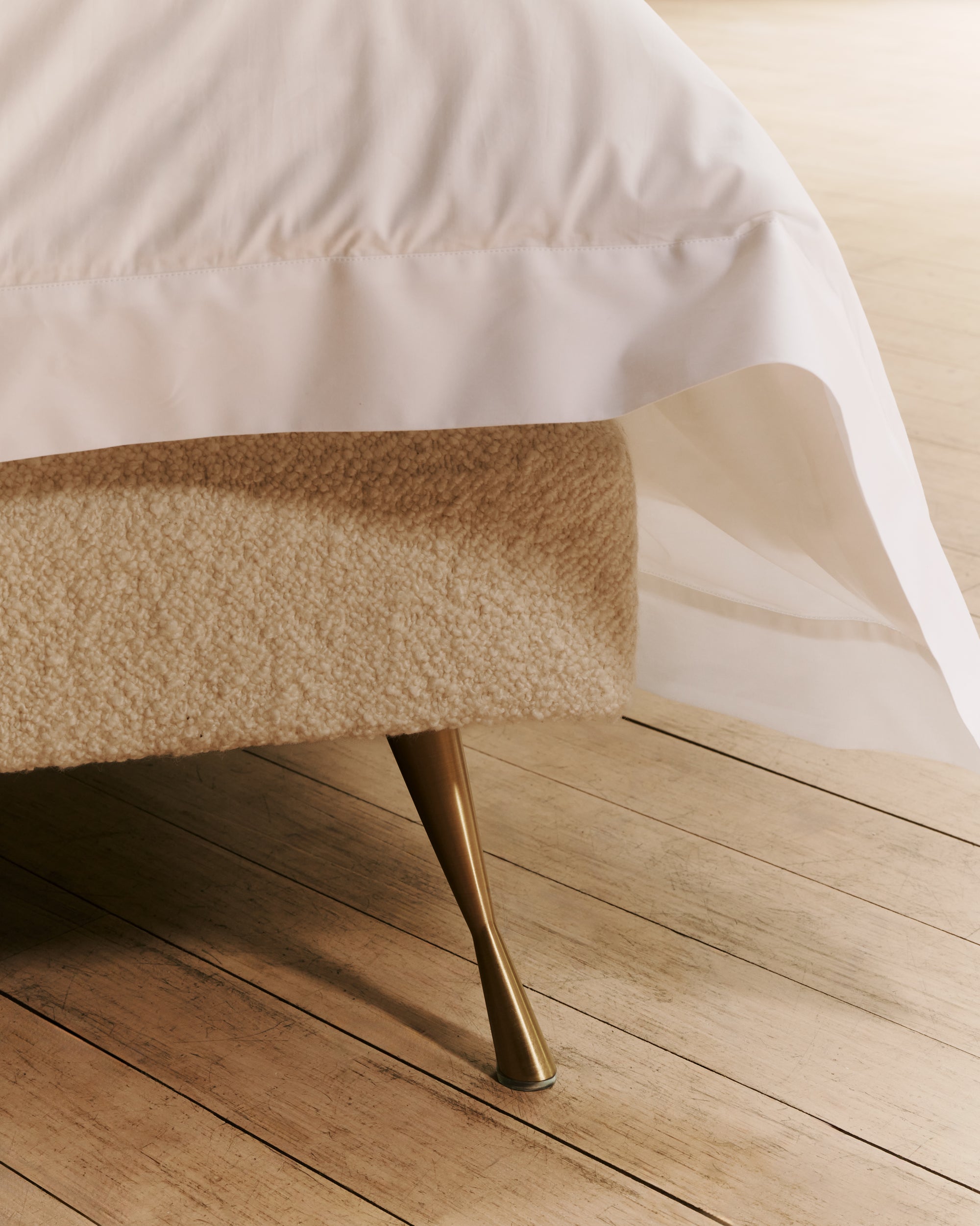 Close-up of the Amelia base with a gold leg on a wooden floor.
