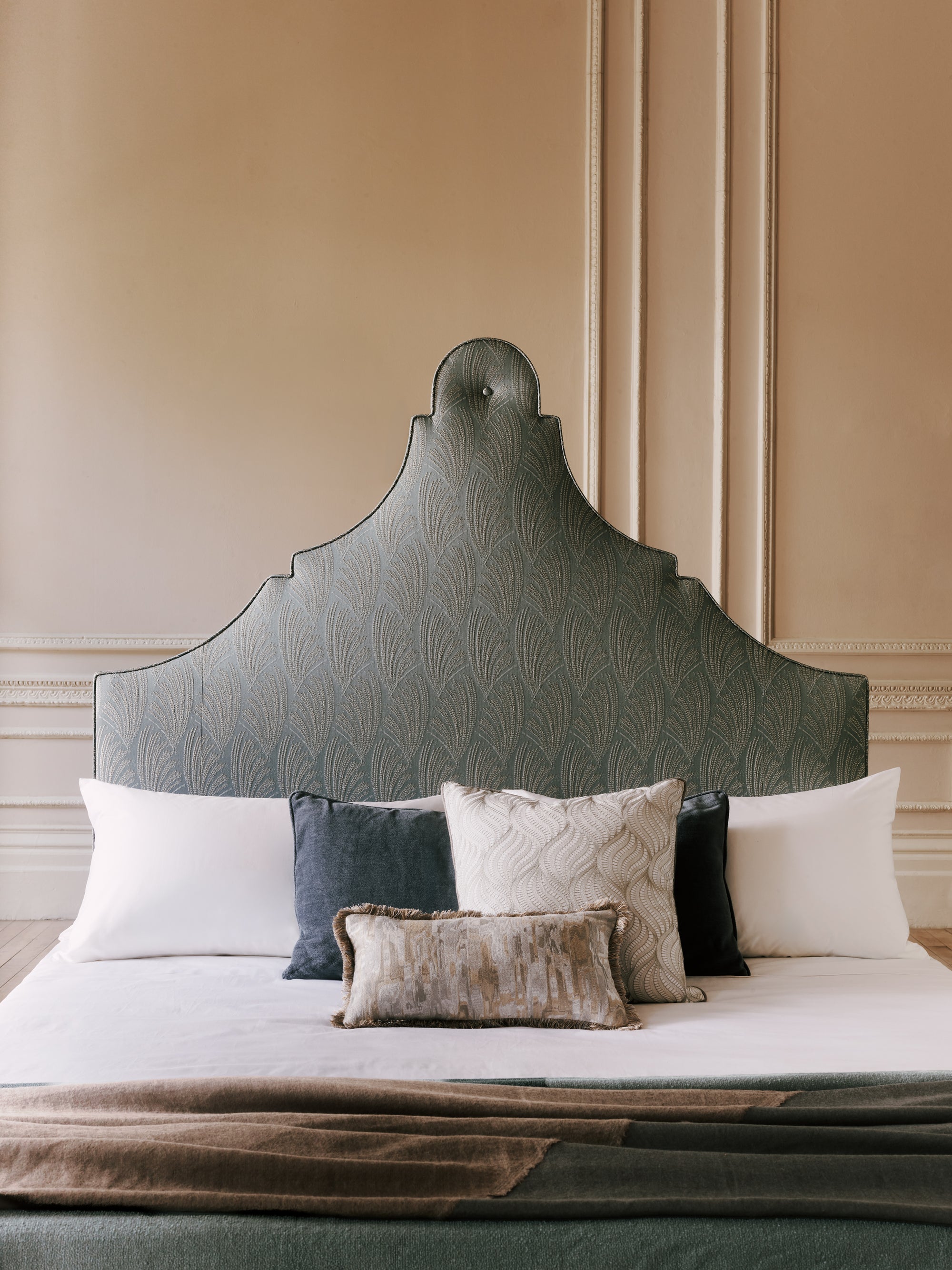 Claudia green headboard with patterned design on a bed with pillows against a beige wall