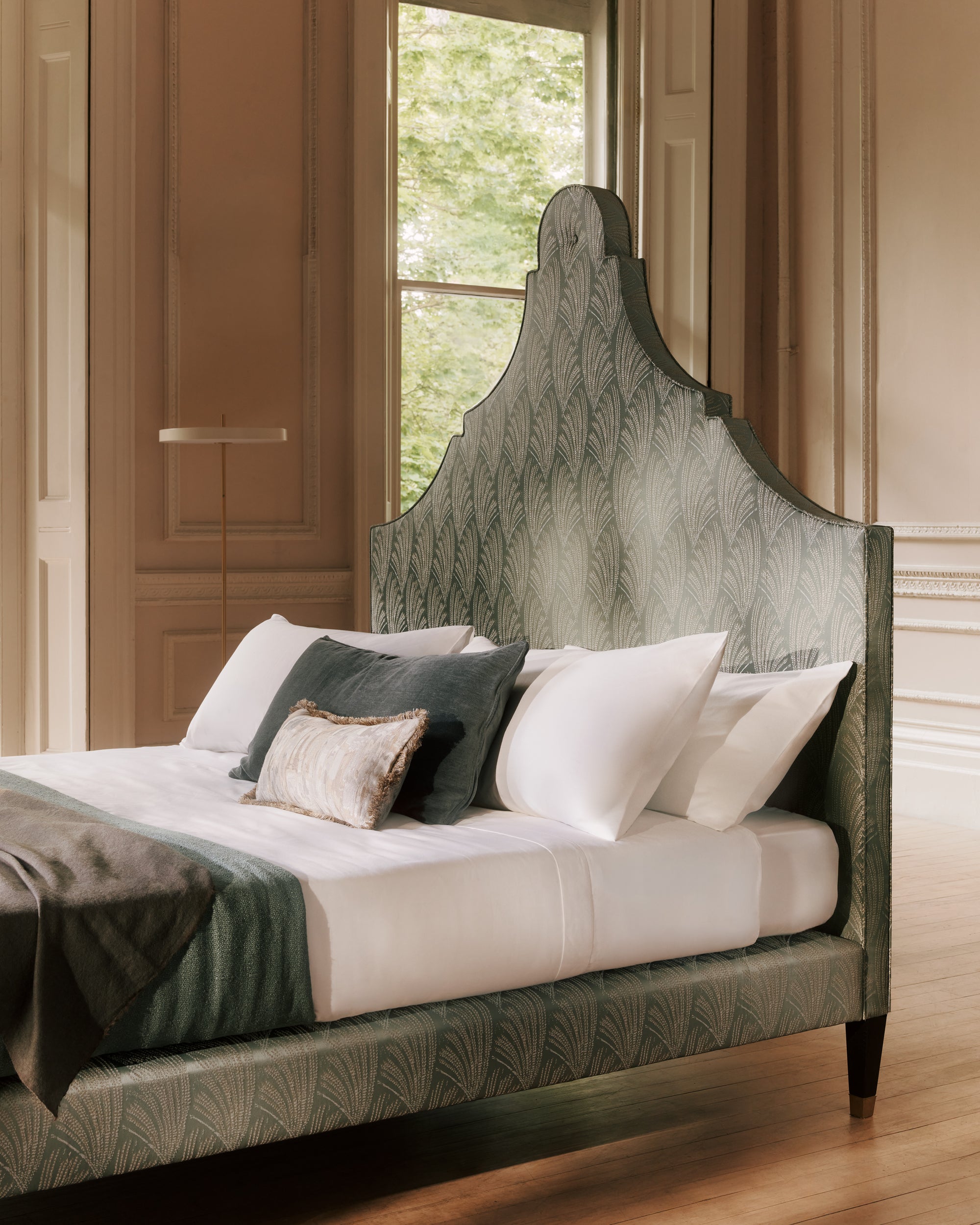 Claudia bed with patterned headboard and pillows in a room with wooden floor 