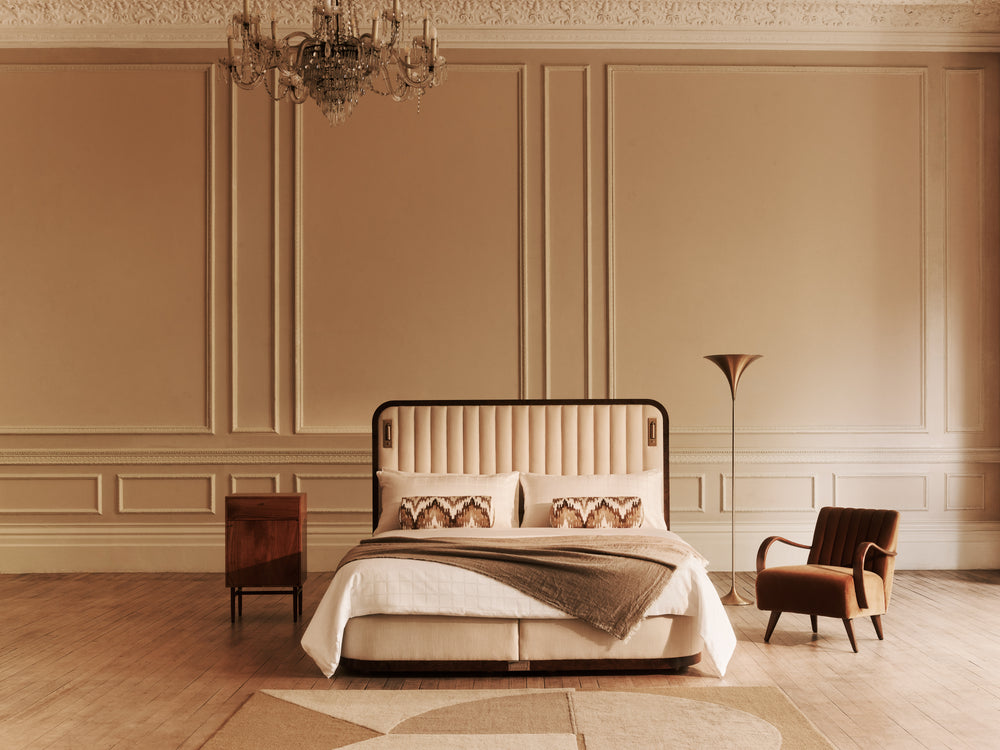 Luxurious bedroom with the Luna bed, an armchair, and chandelier in a warm-toned room.