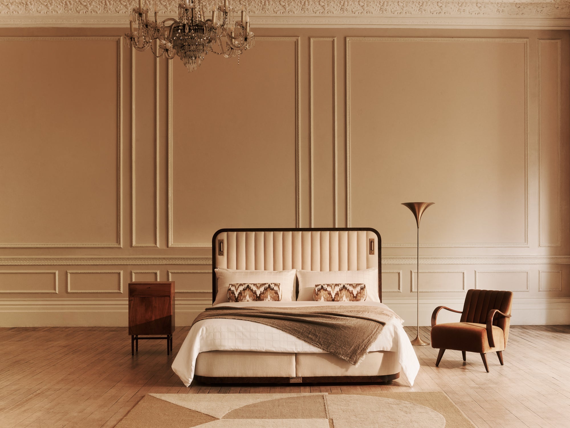 Luxurious bedroom with the Luna bed, an armchair, and chandelier in a warm-toned room.