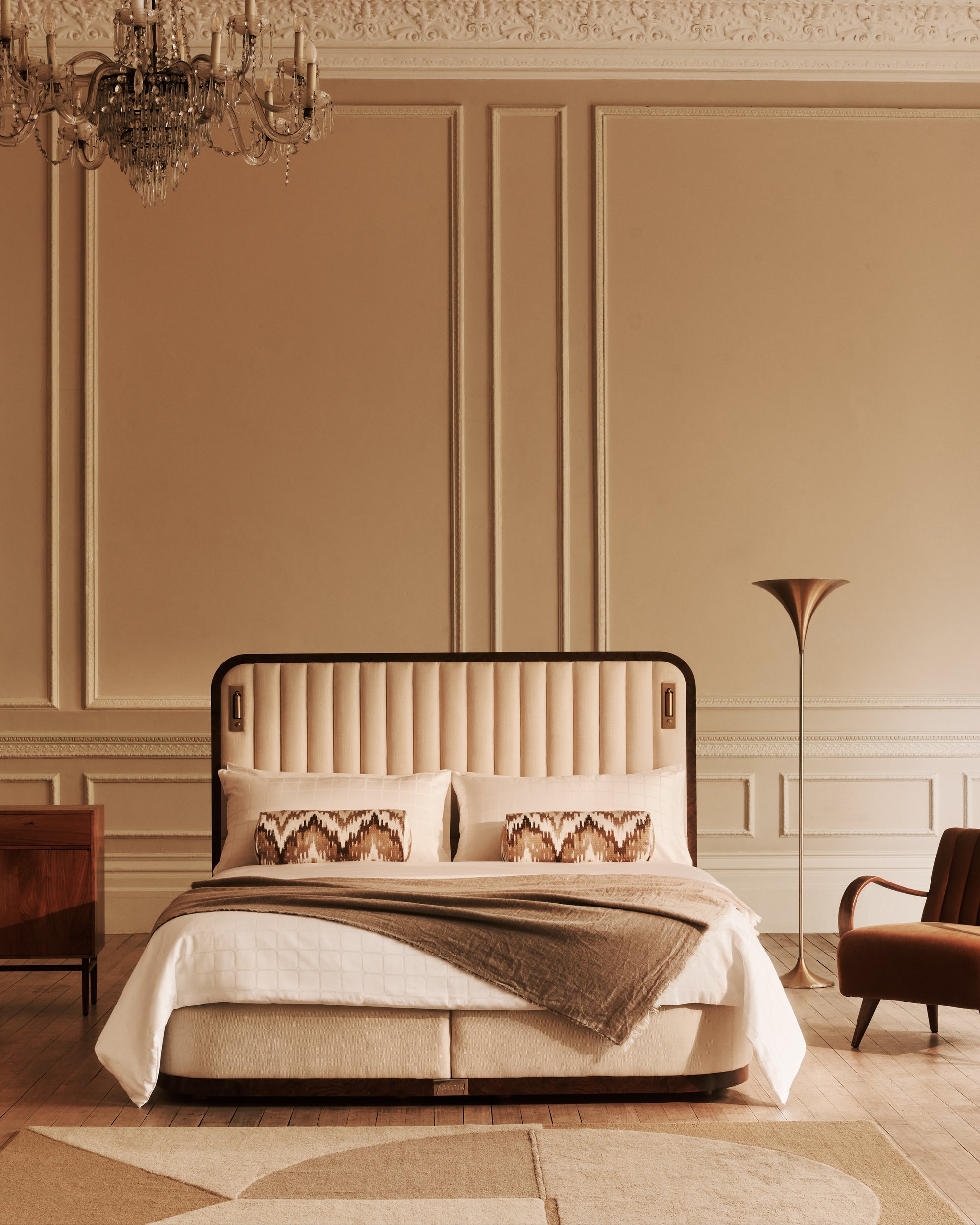 Luxurious bedroom with the Luna bed, armchair, and chandelier in a warm-toned room.