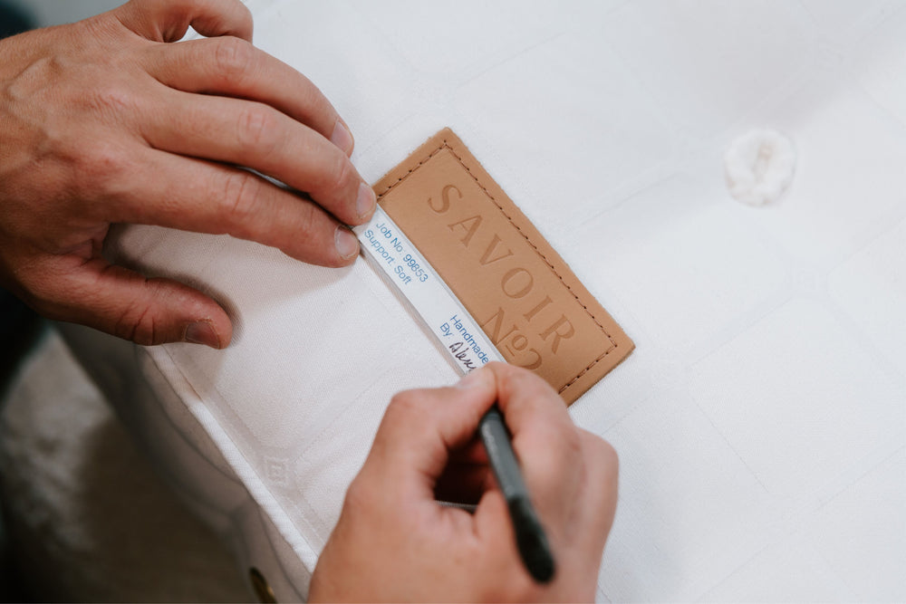 Savoir craftsman using a pen to sign on a 'Savoir' label on stitched on a mattress